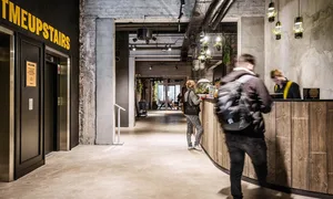 A spacious, industrial-style office interior with concrete walls, steel beams, and exposed brick, featuring a reception desk 