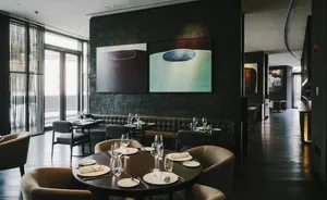 A restaurant interior with dark wood flooring and seating, glassware, and plates on tables, featuring industrial-style artwor