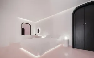 A minimalist bedroom with a white bed on concrete flooring, black wardrobe, and round glass light fixtures.