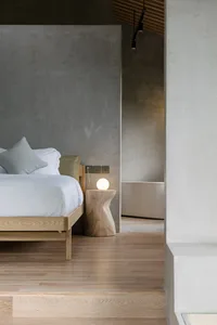 A minimalist bedroom with a wooden bed and light fixture.