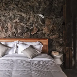 A minimalist bedroom with a wooden bed and a stone wall.