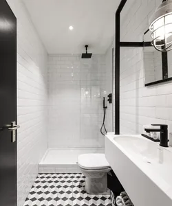 A modern bathroom featuring white subway tiles, a black toilet, and a black and white geometric floor tile pattern.