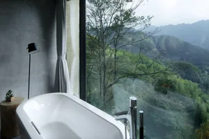 Modern bathroom featuring glass walls and concrete elements with a scenic mountain view.