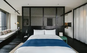 Modern bedroom with a large bed, blue blanket, and minimalist black floor-to-ceiling curtains.