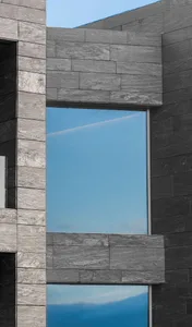 A modern building with a glass window reflecting the blue sky.