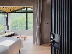 A modern bedroom featuring concrete, wood, and fabric materials, with a large window overlooking greenery.