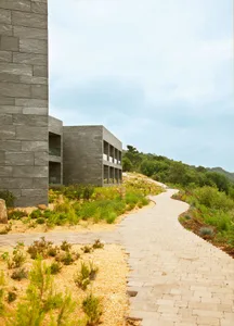 Modern landscape architecture featuring stone structures, gravel pathways, and various plants in a natural setting.