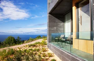 A modern minimalist balcony featuring glass and stone materials with a stunning ocean view.
