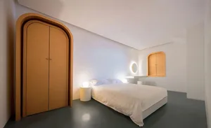 A modern minimalist bedroom with white furniture, a bed, and orange arched doors.