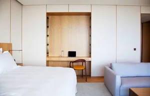 Modern minimalist bedroom featuring a wooden desk and white fabric furniture.