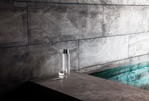Concrete flooring next to a pool with a bottle and glass of water.
