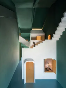 Modern residential interior with vibrant green walls, white and green stairs, and a cozy alcove bedroom.