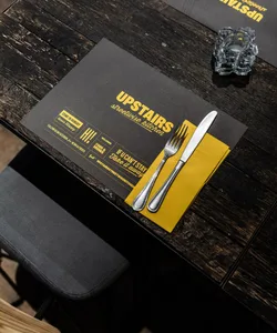 A black placemat with yellow text and a yellow napkin with a fork and knife