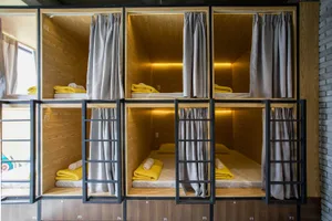 Minimalist design of hostel sleeping quarters with wooden elements and gray curtains.