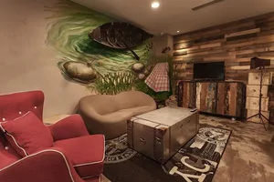 A cozy industrial-style living room with a retro trunk as a centerpiece, wooden panel walls, and a mural of a fishing boat on