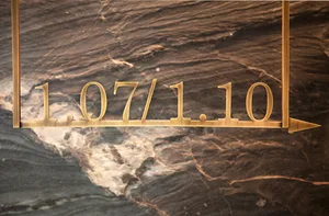 Gold-colored metal sign with date and arrow on marble background