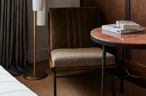 A modern bedroom with a fabric upholstered chair, wooden table, and marble top.