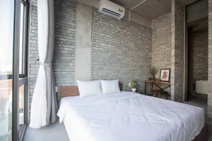Modern bedroom with exposed brick walls, white bedding, and a large window