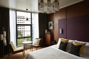 A modern hotel room featuring wooden paneling, fabric bedding, and metal accents.