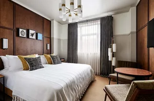 Modern hotel room featuring wooden walls, a white bed, and a metal table with chairs.