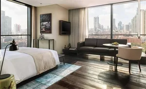 A modern hotel suite featuring a bed, sofa, and cityscape view.