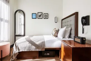 A minimalist bedroom featuring a bed with a tufted headboard and white bedding, a mirrored floor lamp, and wall art in neutra