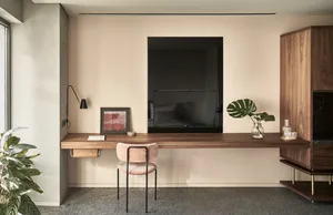 A minimalist home office with a wooden floating desk, a pink upholstered chair, a framed abstract art piece, and a monstera l