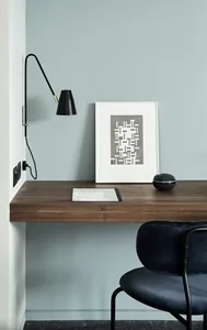 Minimalist office workspace featuring a wooden desk, a black swing arm lamp, and a framed abstract geometric print.