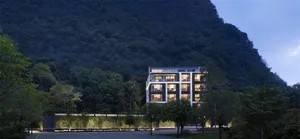 A modern apartment building with glass and concrete exterior and steel accents, located near a forested hillside.