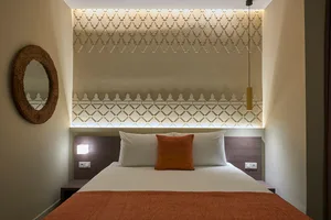 Modern bathroom with white and orange bedding on a bed, textured white walls, and a round mirror.