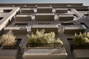 Modern concrete building facade with balconies and greenery.