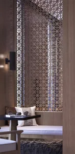 A modern living space featuring wooden paneling with intricate laser-cut patterns, a cushioned bench, and a small table with 