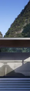 A modern architectural design featuring concrete steps and a concrete wall with a water feature, set against a natural mounta