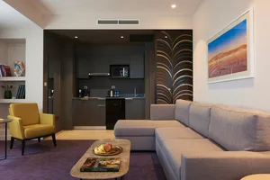 A modern living room with a grey fabric sectional sofa, a yellow upholstered armchair, a coffee table with a fruit bowl and a