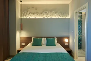 Modern minimalist bedroom with turquoise bedding, white walls, and wooden headboard.
