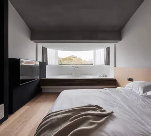 A modern minimalist bedroom with concrete walls, wood flooring, and a large window.