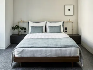 Modern minimalist bedroom featuring a wooden bed frame with metal handles, white bedding, and dark grey accents.