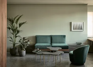 Modern minimalist living room featuring green velvet couches, concrete floor, and minimalistic decor.