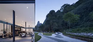 A modern resort pathway featuring natural stone elements surrounded by lush greenery and rocky formations.