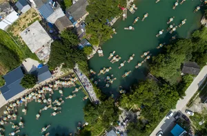 Aerial view of a river township with colorful boats, green trees, and traditional buildings
