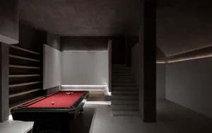 A minimalist industrial game room featuring a red pool table, concrete walls, and a lamp.