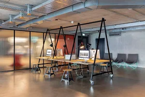 Modern industrial office workspace with concrete walls, wooden desks, and metal frame tables.