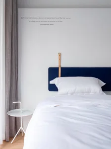 A minimalist bedroom featuring a blue upholstered bed with a white bedspread, white bedside table, and minimalist decor.