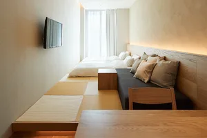 Minimalist living room featuring a sofa with pillows, a coffee table, tatami mats, and a television mounted on the wall.