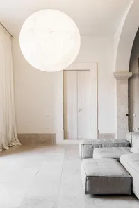 A minimalist living space featuring a sofa, ottoman, and large spherical light fixture.