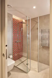 Modern bathroom with red patterned tile walls and a glass shower enclosure.