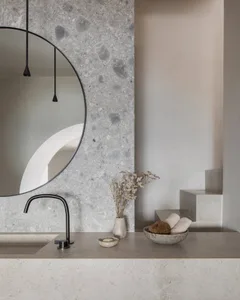 Modern minimalist bathroom featuring a circular mirror mounted on a terrazzo wall, a floating vanity, and dried flowers in a