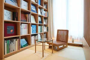 A modern room with a wooden bookshelf, rattan chair, and glass table.