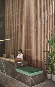 A modern lobby interior featuring a marble desk with a green cushion and a wooden grille wall behind it.