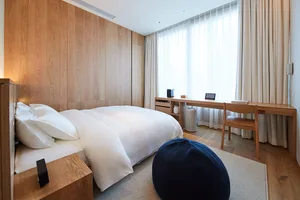 A modern minimalist bedroom featuring wood walls, a white bedspread, and a navy pouf.